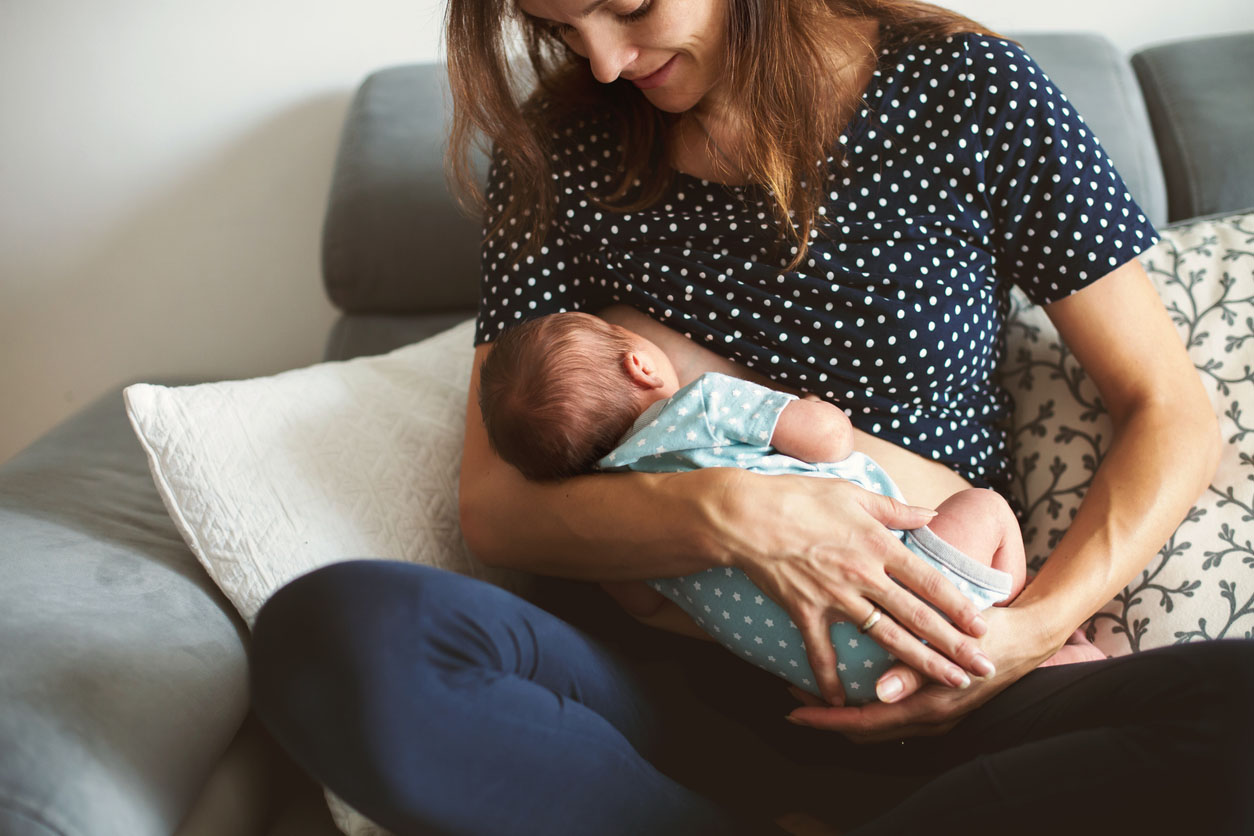 Une Jeune Mère Moderne Qui Donne Du Lait À Son Bébé De La Bouteille, Un Bébé  Sans Soucis Dans Les Bras De La Mère Qui Boit Du Lait Chaud À Partir D'une