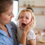 Une mère retenant une fille pleurante d’enfant en bas âge à l’intérieur dans la cuisine
