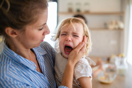 Une mère retenant une fille pleurante d’enfant en bas âge à l’intérieur dans la cuisine