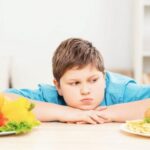 enfant obese devant deux assiettes de nourriture