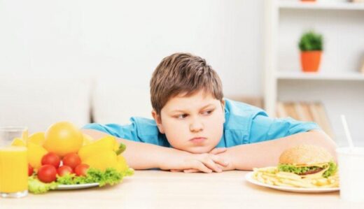 enfant obese devant deux assiettes de nourriture