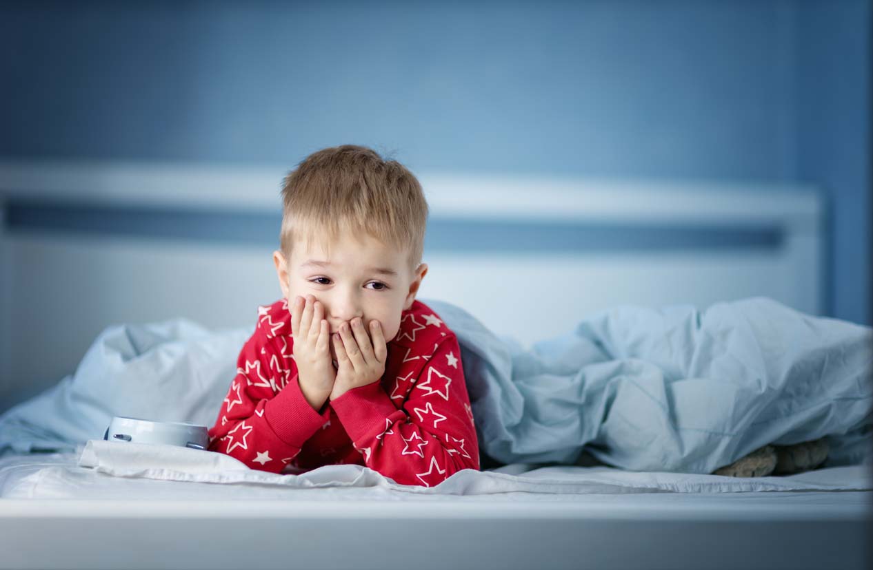 Garçon somnolent se trouvant dans le lit avec les literies bleues