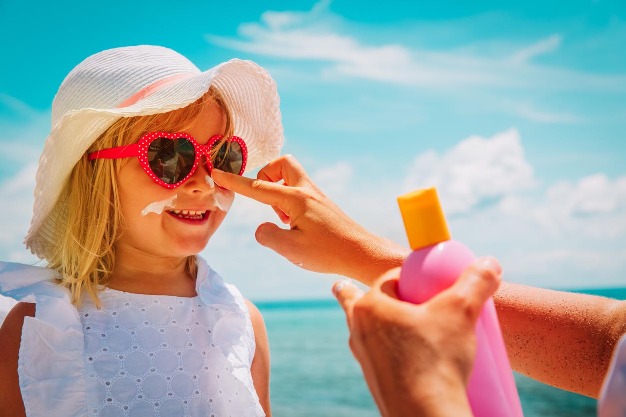 Mère a mis la crème écran solaire sur le petit visage de la fille à la plage