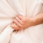 Main féminine agrippant sur un lit blanc, signe de l’orgasme de la femme