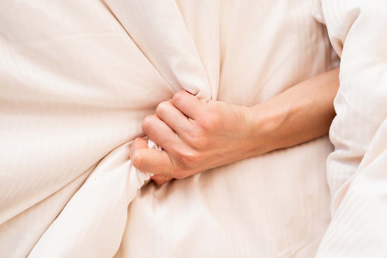 Main féminine agrippant sur un lit blanc, signe de l’orgasme de la femme